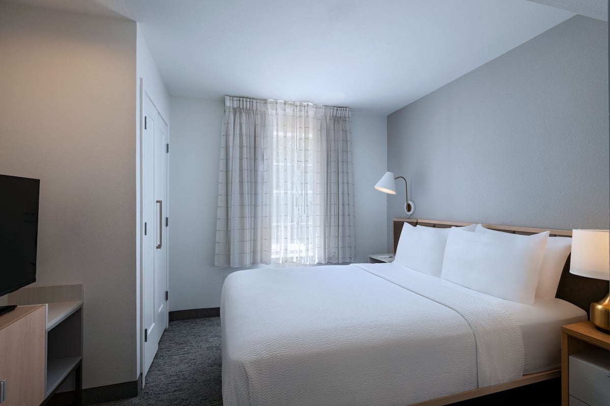 Een hotelkamer met een bed, een televisie, een bureau en een raam met gordijnen.