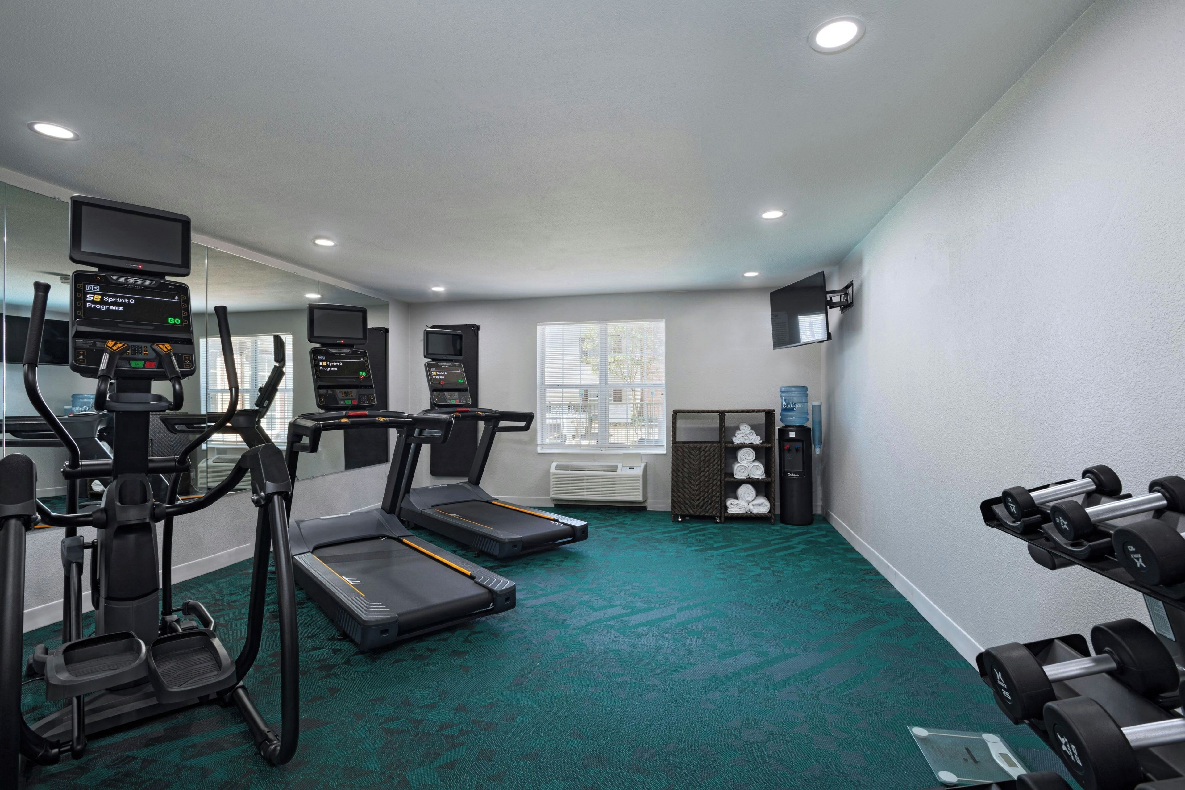 A fitness room with treadmills, a stationary bike, and dumbbells.