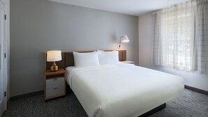 A hotel room with a large bed, two bedside tables with lamps, a window with curtains, and a carpeted floor. - TownePlace Suites by Marriott College Station (College Station)
