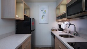 A compact kitchen with a refrigerator, microwave, sink, and a framed artwork on the wall. - TownePlace Suites by Marriott College Station (College Station)
