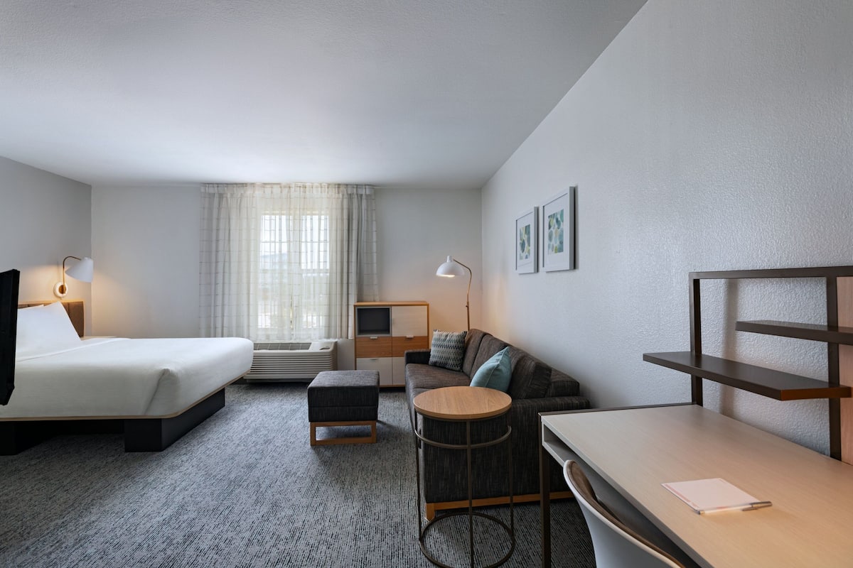 Een hotelkamer met een bed, een slaapbank, een bureau, een stoel, een bijzettafeltje, een lamp, een televisie en een raam met gordijnen.