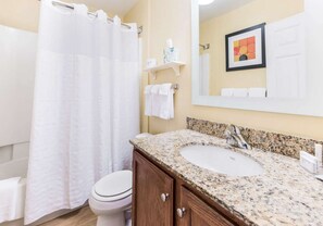 A bathroom with a white toilet, a granite sink, a shower curtain, and a towel rack.