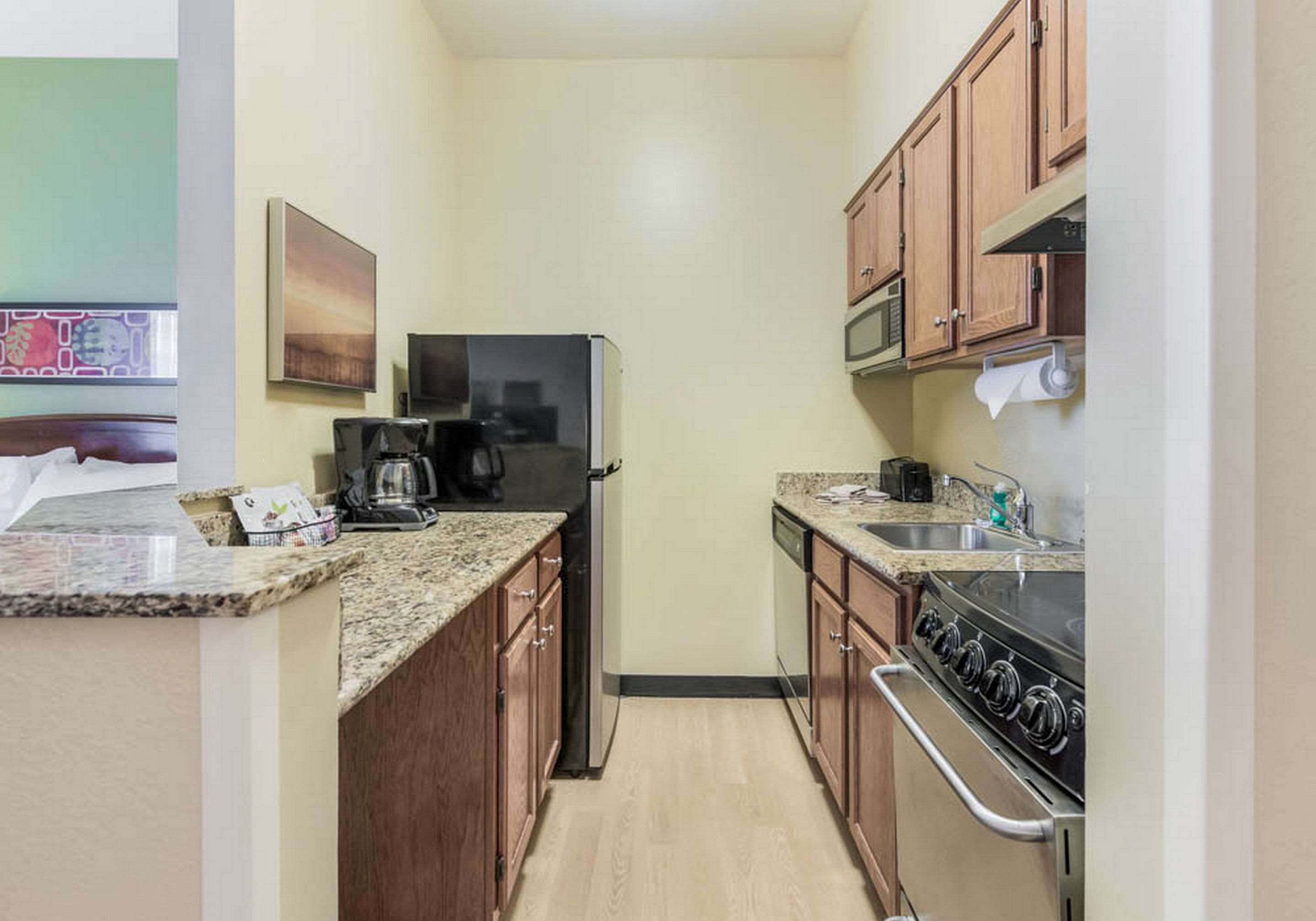 A compact kitchen with wooden cabinets, a refrigerator, a microwave, a stove, and a coffee maker.