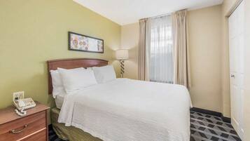 Quarto de hotel com cama, mesa de cabeceira com telefone, abajur e janela com cortinas.