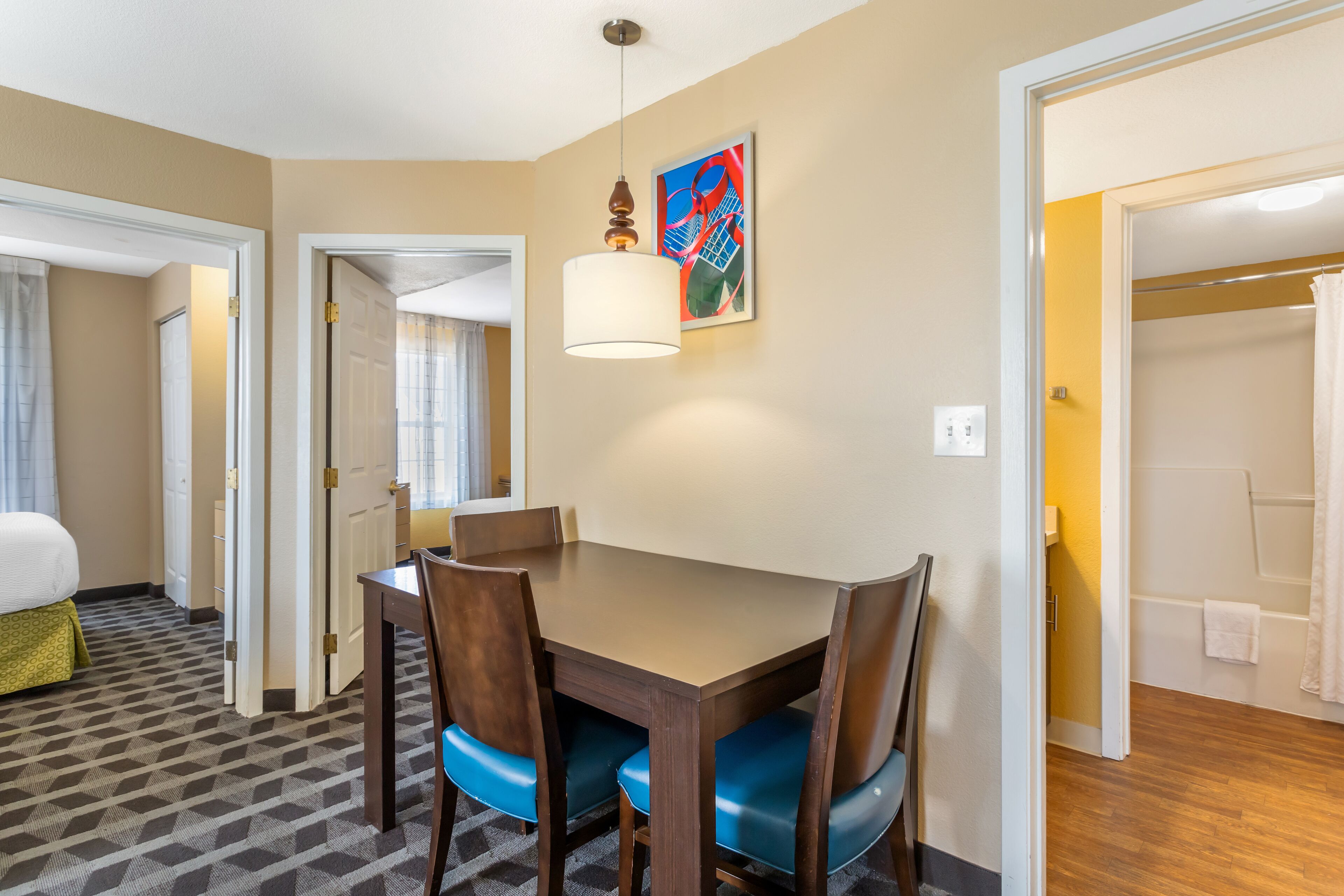 A hotel room with a dining table, chairs, a bed, and a bathroom visible through an open door.
