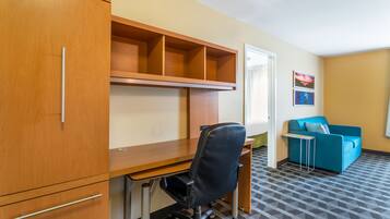 A room with a wooden desk, a black office chair, a blue sofa, and a patterned carpet.