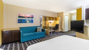 A hotel room with a bed, a blue sofa, a desk with a chair, a TV, and artwork on the wall. - MainStay Suites Houston NASA/Clear Lake (Houston)