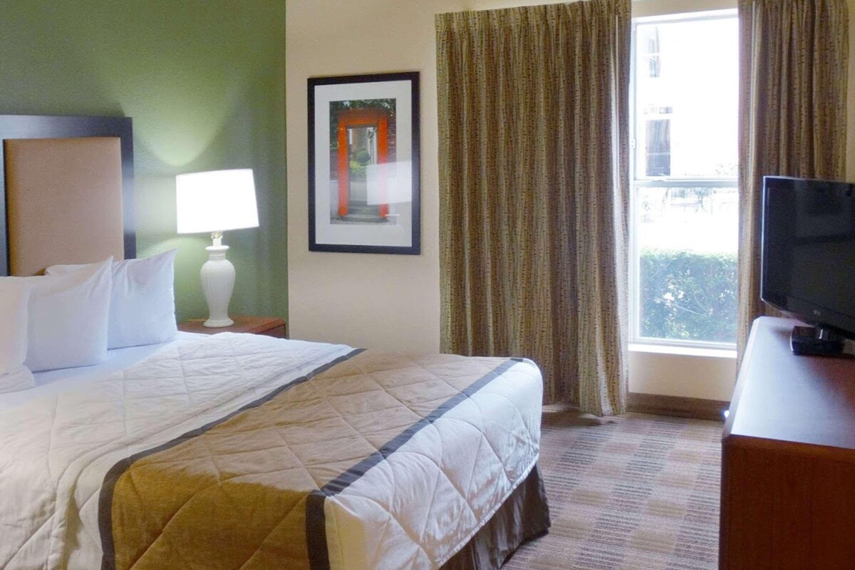 A hotel room with a bed, a television, a framed picture, and a window with curtains.
