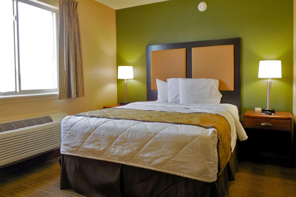 Una camera d'albergo con un letto, due lampade sui comodini, una finestra con tende e un riscaldatore a parete.