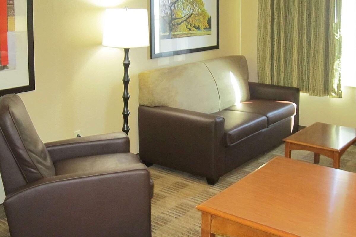 A living room with a sofa, armchairs, a lamp, a table, and a framed picture on the wall.