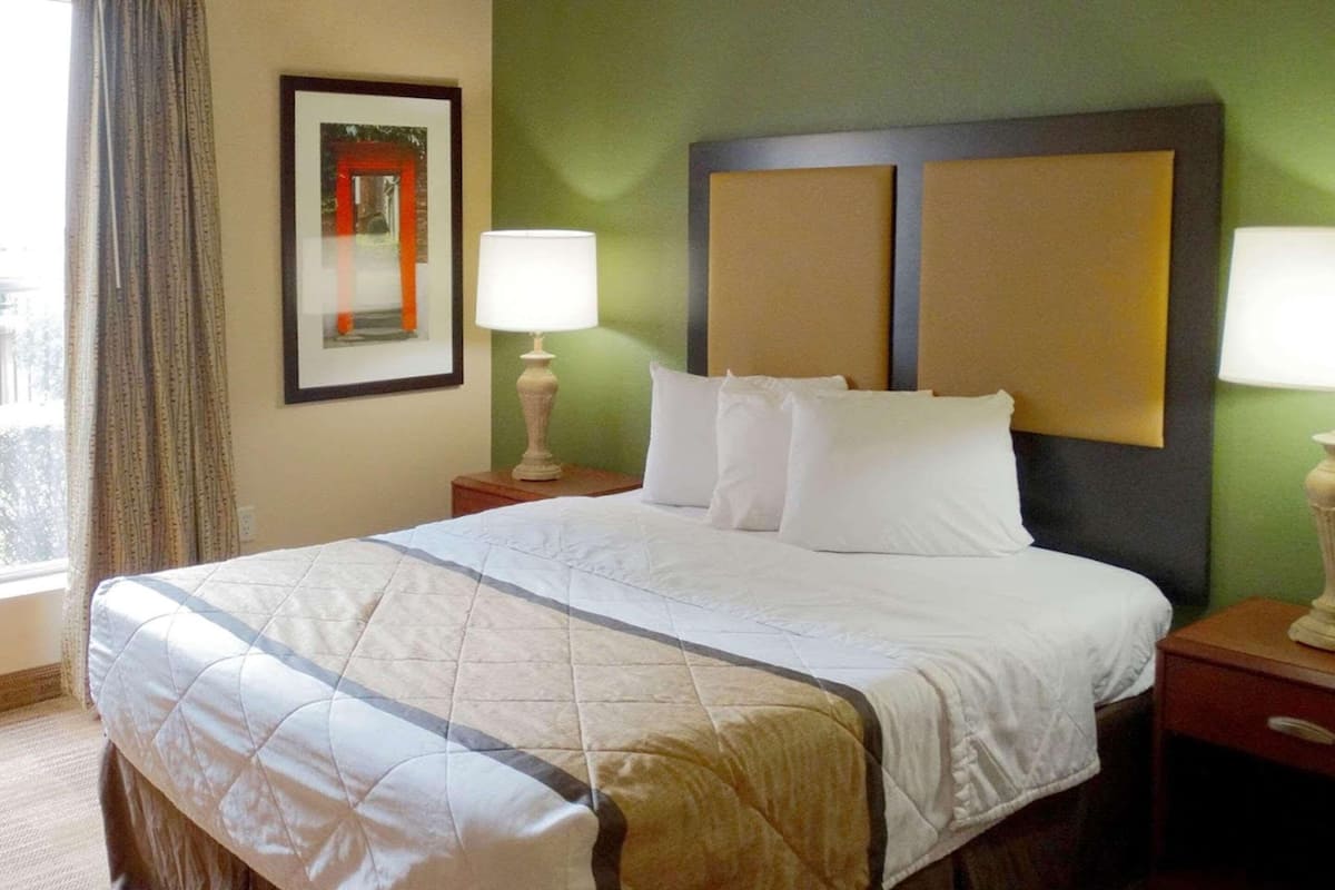 Una camera d'albergo con un letto, due comodini, un quadro appeso alla parete e una finestra con tende.