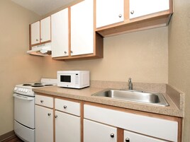 Una cocina con armarios blancos, estufa, microondas y pileta de acero inoxidable.