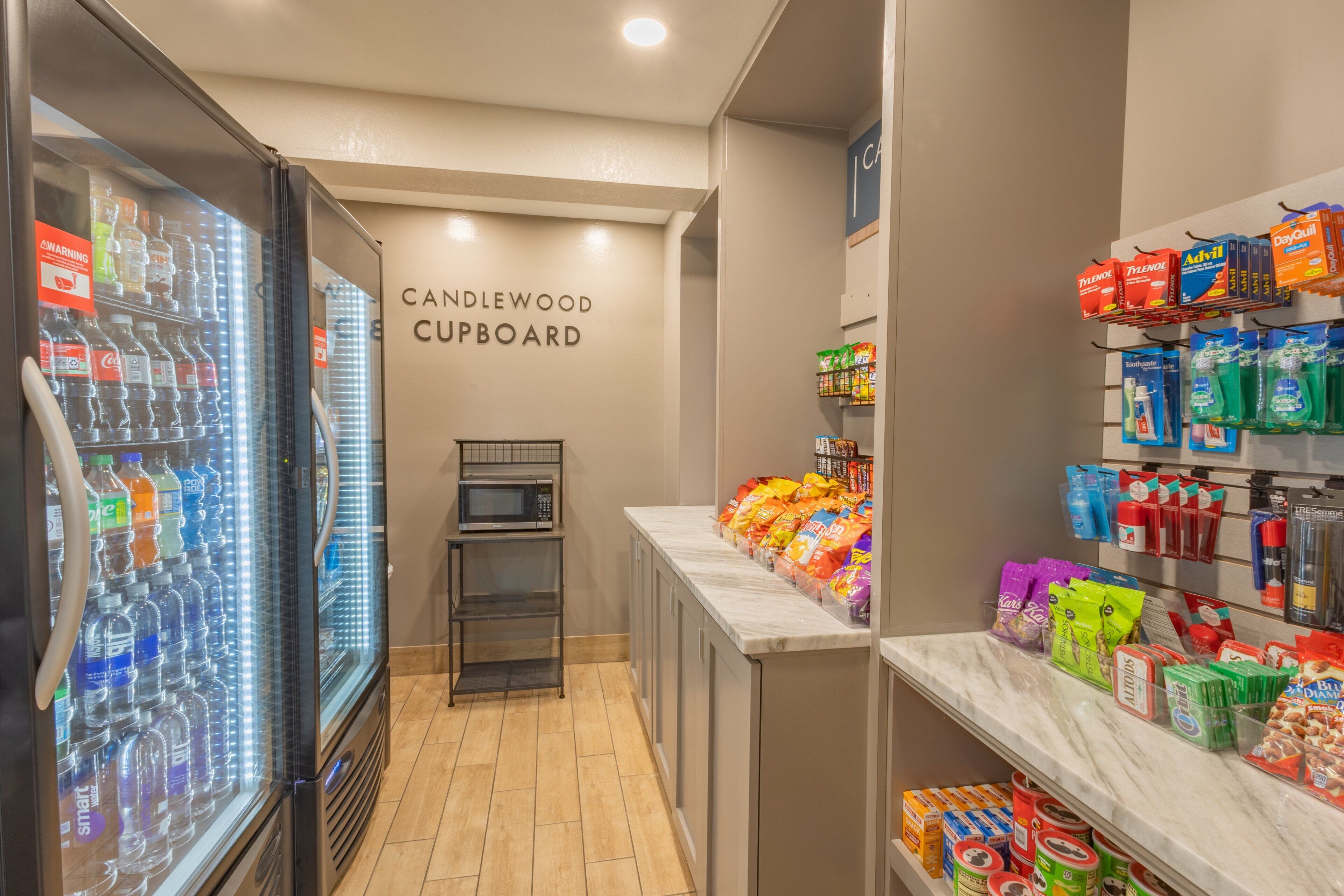 A kitchenette area with a refrigerator, microwave, and a shelf with snacks and beverages.
