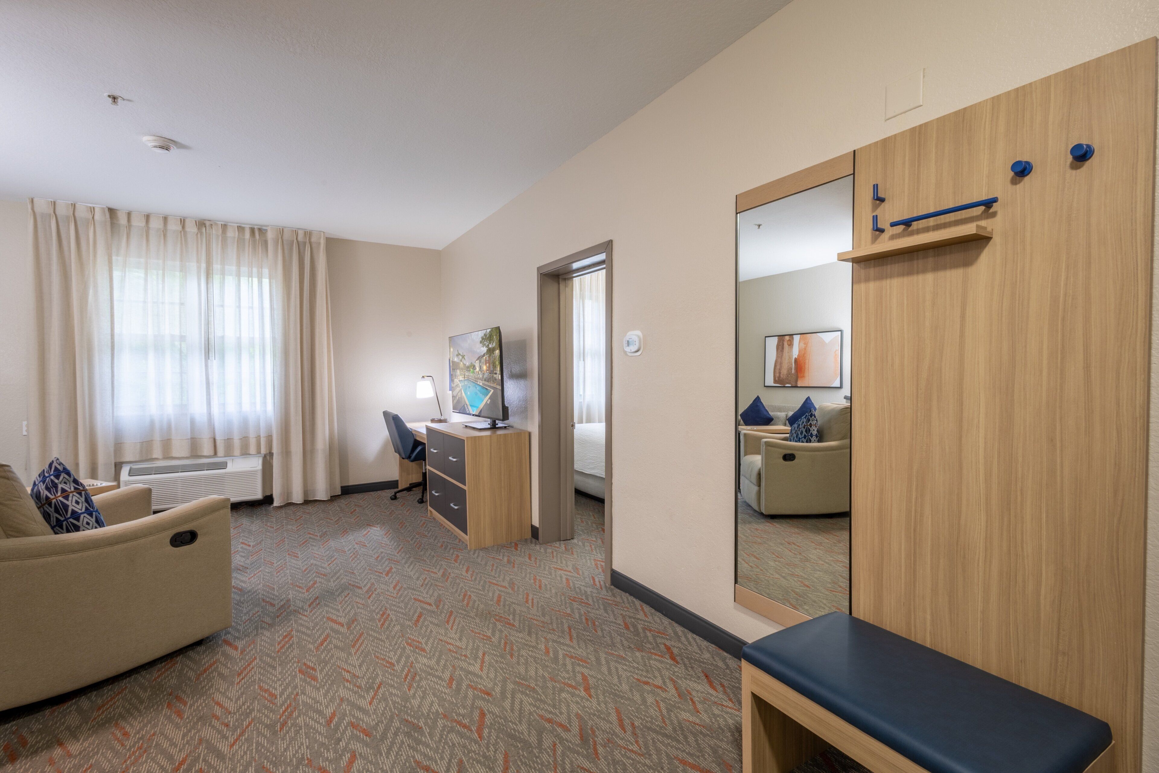Una habitación de hotel con sofá, escritorio con computadora, cama, espejo y armario.