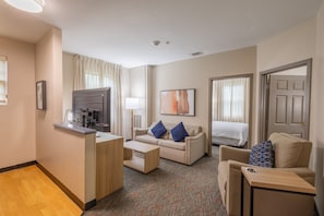 Habitación de hotel con kitchenette, sofá, sillón, cama y televisor.