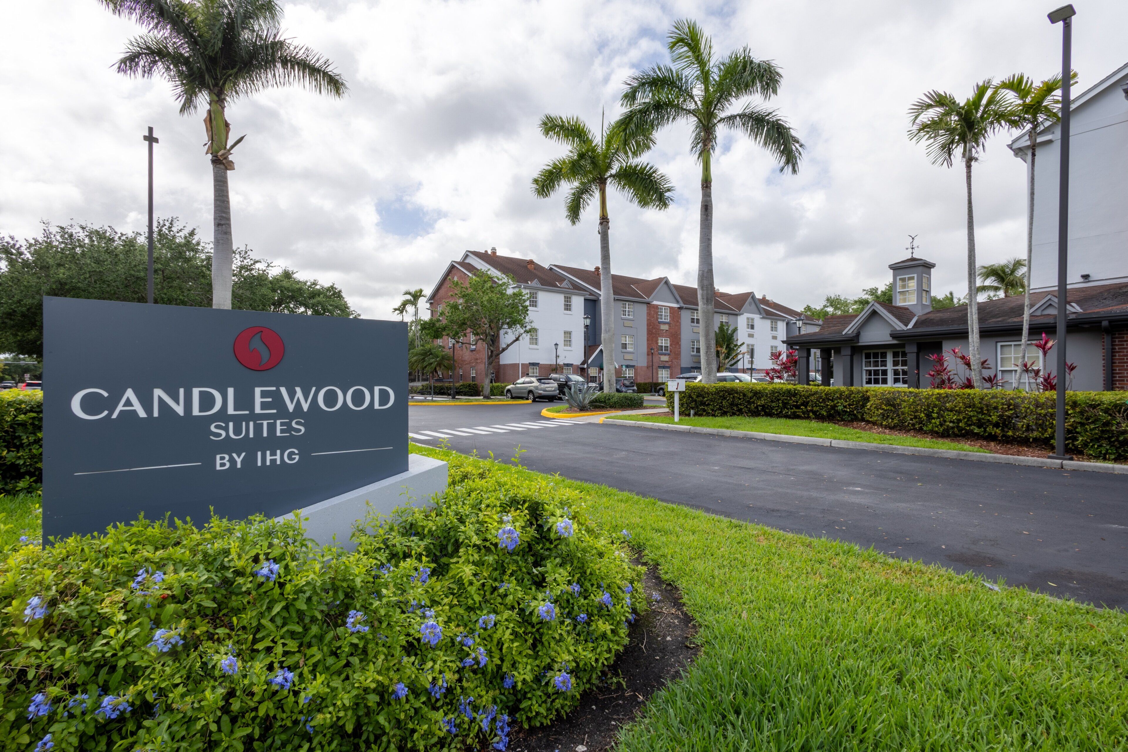 Une enseigne de l’hôtel Candlewood Suites, appartenant au groupe IHG, entourée de verdure et de palmiers.