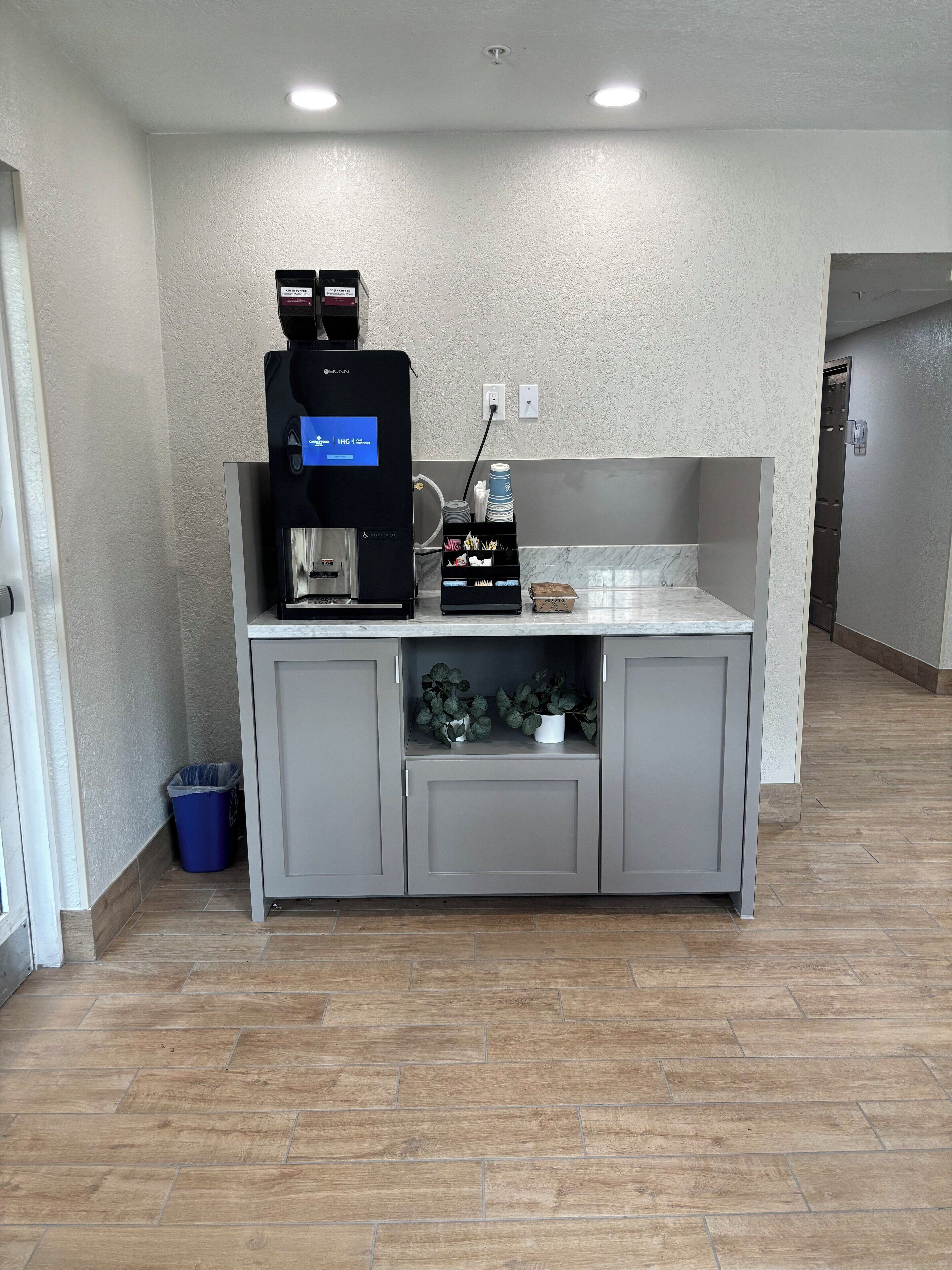 A kitchenette area with a coffee machine, a small plant, and a trash bin.