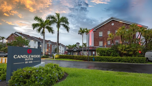A hotel entrance with a sign for Candlewood Suites by IHG, surrounded by greenery and palm trees. - Candlewood Suites Miami Lakes by IHG (Miami Lakes)