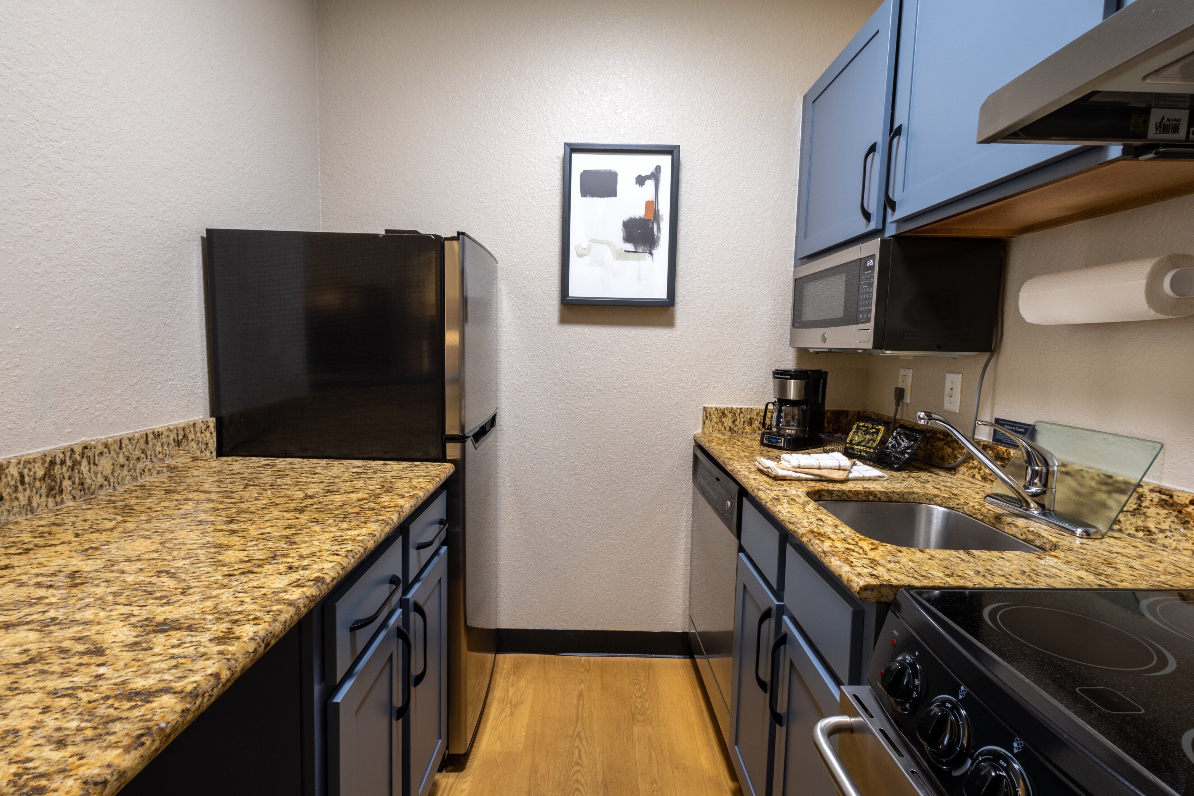 A compact kitchen with granite countertops, a stainless steel refrigerator, a microwave, a stove, and a sink.