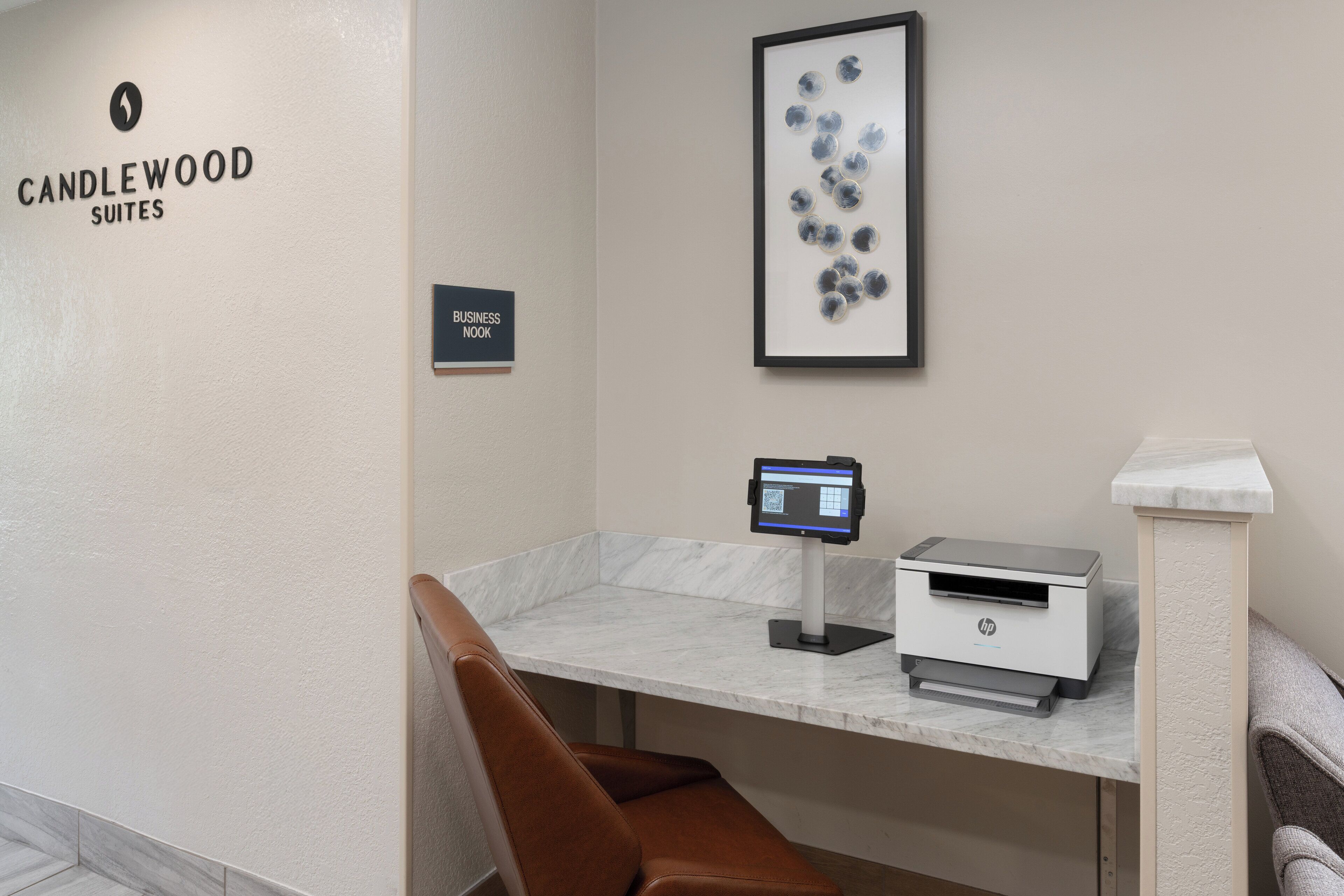 A business nook in Candlewood Suites with a marble counter, an HP printer, and a framed abstract art piece.