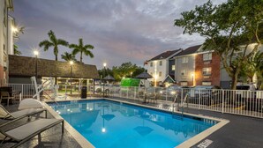 A swimming pool with lounge chairs, a fenced deck area, and a building with a brick facade. - Candlewood Suites Miami Lakes by IHG (Miami Lakes)