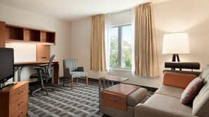 A hotel room with a desk, chair, sofa, TV, lamp, and window with curtains.