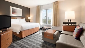 A hotel room with a bed, a sofa, a TV, a desk, and a window with curtains.