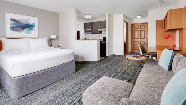 Ein Hotelzimmer mit einem großen Bett, einer Schlafcouch, einem kleinen Tisch und einer Küchenzeile.