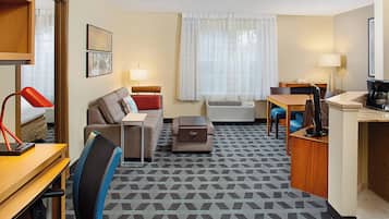 Habitación de hotel con sofá, escritorio, silla, lámpara y cafetera.
