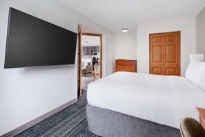 A hotel room with a bed, a TV mounted on the wall, a wooden wardrobe, and a desk with a chair. - Towneplace Suites by Marriott Horsham (Horsham)