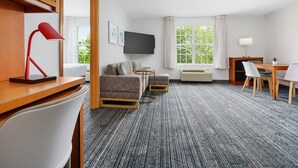 Ein Hotelzimmer mit Sofa, Sessel, kleinem Tisch, Fernseher, Schreibtisch mit Stuhl und einem Vorhang vor dem Fenster.