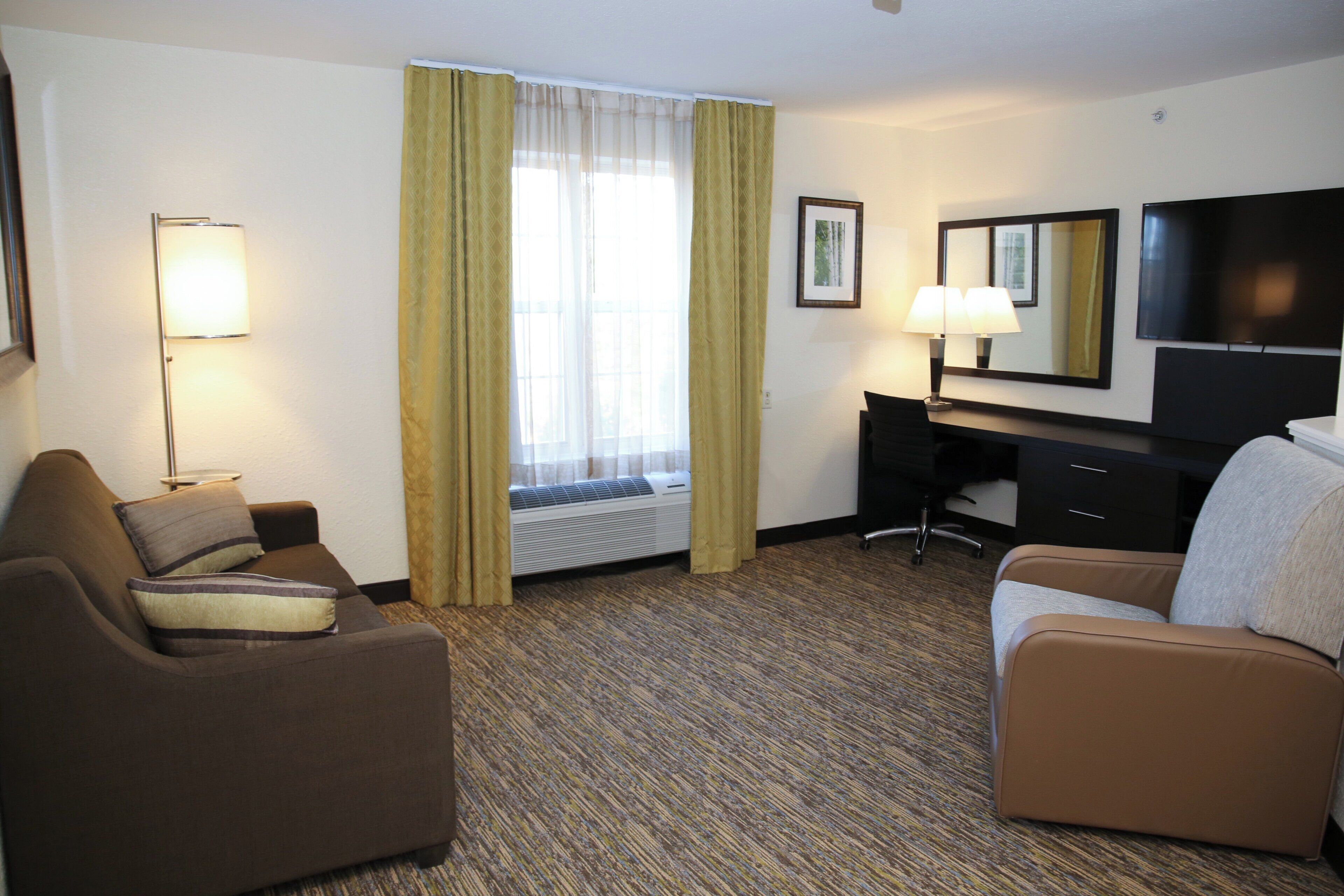 Une chambre d’hôtel avec un lit, un bureau, une chaise, une télévision et une fenêtre avec des rideaux.