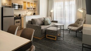 A modern hotel room with a kitchenette, a sofa, a dining table, and a chair.