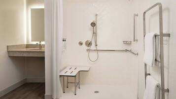 A modern bathroom with a shower, a sink, and a small stool.
