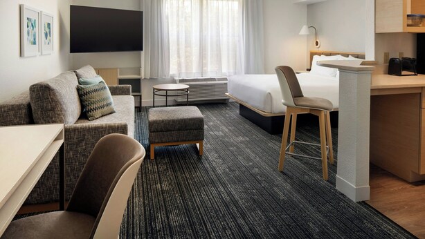 A hotel room with a bed, a desk, a chair, a sofa, a TV, and a window with curtains.