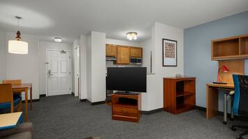 Habitación de hotel con televisión de pantalla plana, armarios de madera, escritorio con silla, estantería y zona de comedor con mesa y sillas.