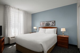 A hotel room with a large bed, two bedside tables with lamps, a flat-screen TV, and a window with sheer curtains.