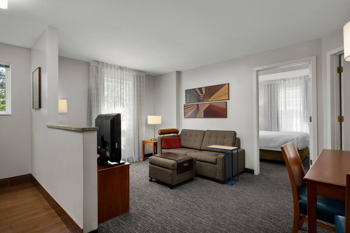 Habitación de hotel con sofá, reposapiés, televisión, lámpara y cama.