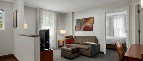 Habitación de hotel con sofá, reposapiés, televisión, lámpara y cama.