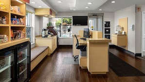 A modern hotel lobby with a reception desk, seating area, and a refrigerator stocked with snacks.