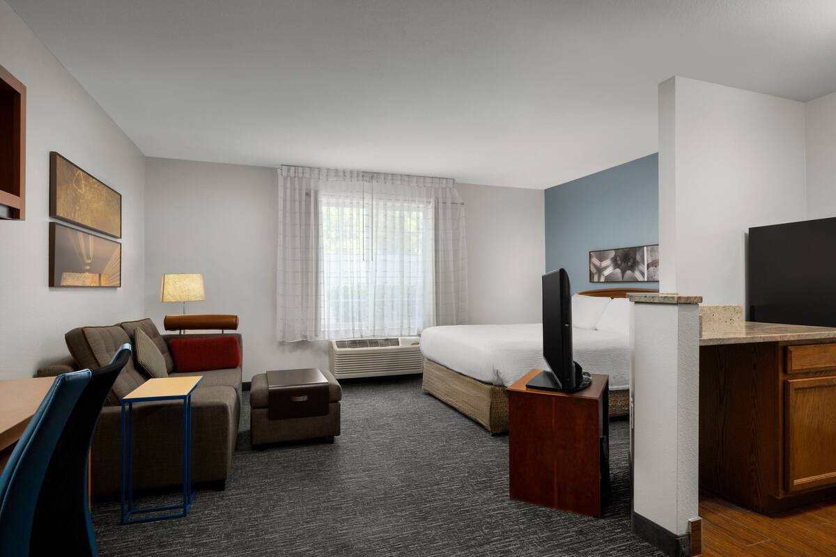 Una habitación de hotel con cama, escritorio, silla, televisor y ventana con cortinas.