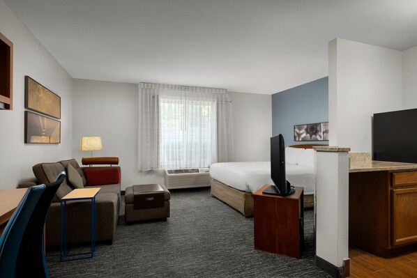 A hotel room with a bed, a desk, a chair, a TV, and a window with curtains.