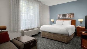 A hotel room with a bed, bedside lamps, a TV, a desk, and a window with sheer curtains.