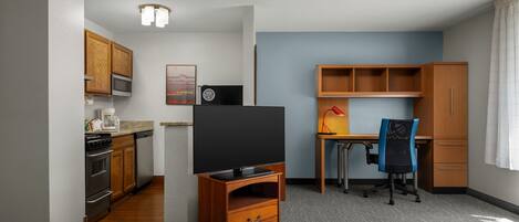 A compact hotel room with a kitchenette, a desk with a chair, and a television.