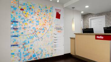 Un área de recepción con un mapa de colores en la pared, un cartel que dice 'Hello' y un tablón de anuncios con un mensaje de bienvenida.