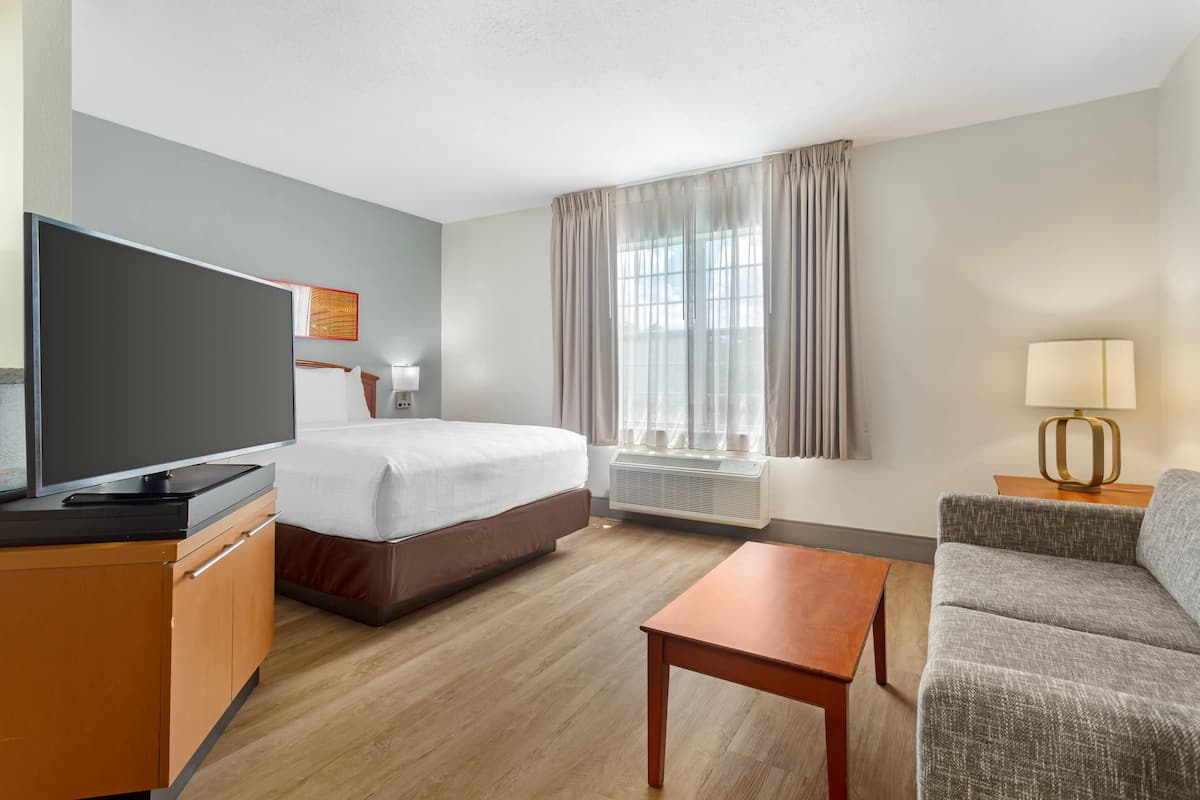 A hotel room with a bed, a TV, a desk, a sofa, and a window with curtains.