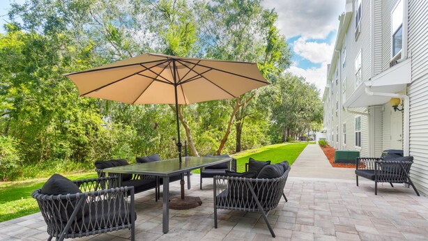 Un patio al aire libre con una mesa y sillas, rodeado de piso de ladrillo y follaje.