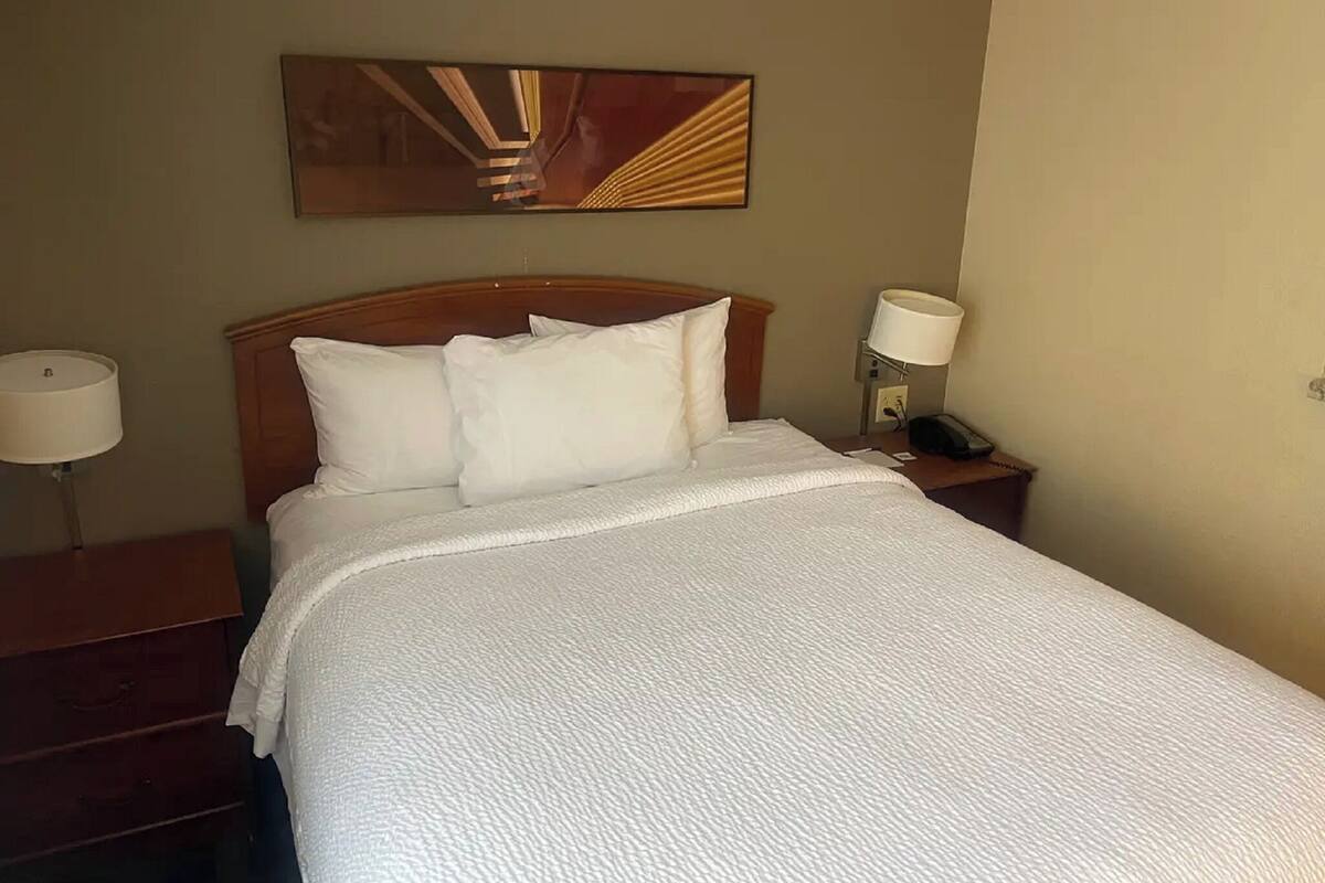 A hotel room with a bed, two bedside tables, a lamp, and a wall-mounted artwork.