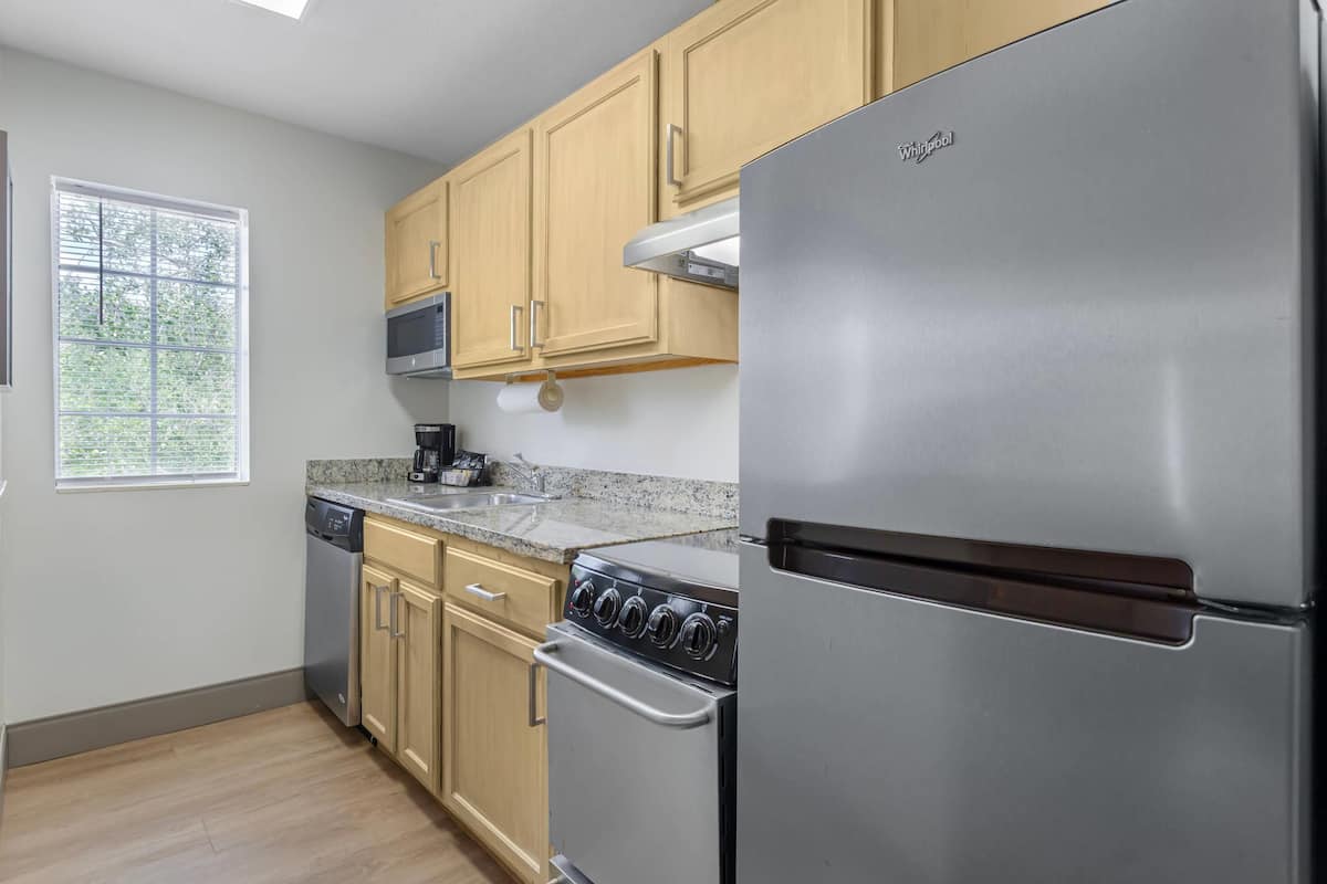 A modern kitchen with stainless steel appliances, wooden cabinets, and a window providing natural light.