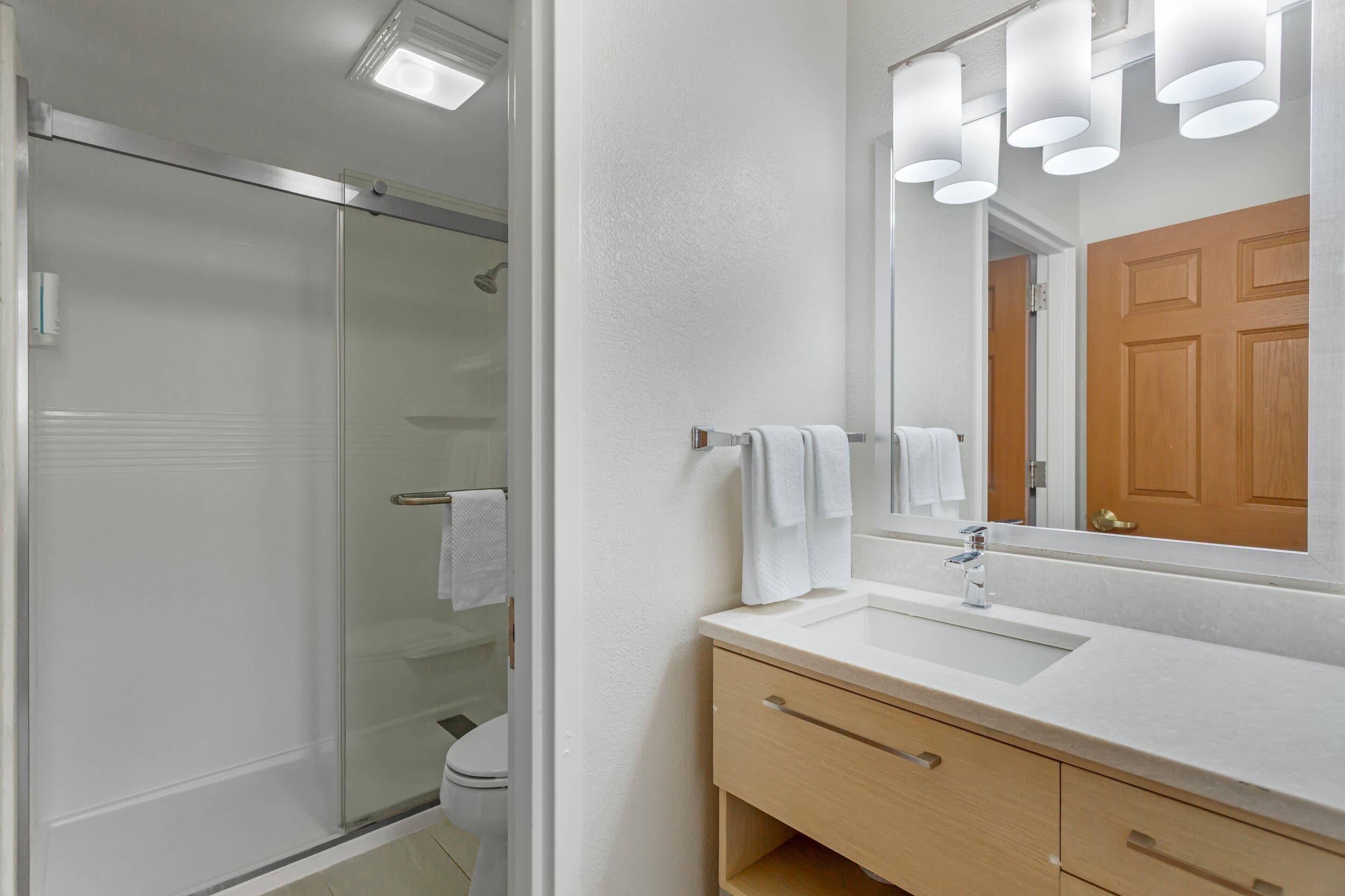 Un baño moderno con cabina de ducha de vidrio, un lavamanos blanco y un mueble de tocador de madera.